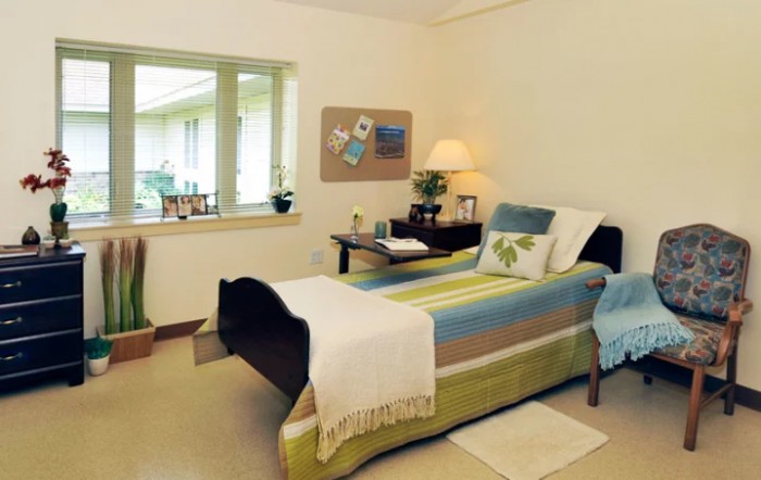 A cozy bedroom with a single bed, a window, and warm lighting from a bedside lamp.