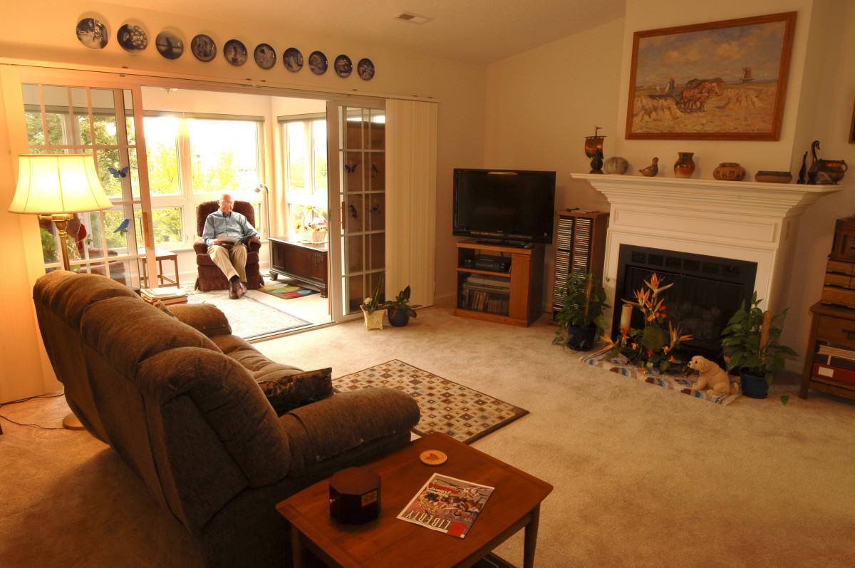 A cozy living room with a sofa, television, and fireplace, where a person is relaxing near large windows.
