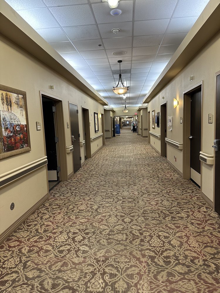 A long, carpeted hallway with doors on either side and paintings on the walls.