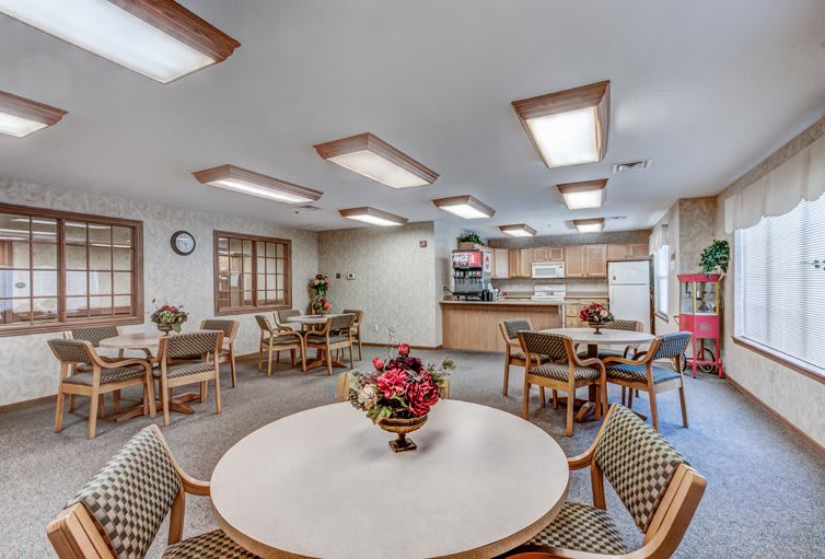 A communal dining area with tables, chairs, and a kitchen in the background.