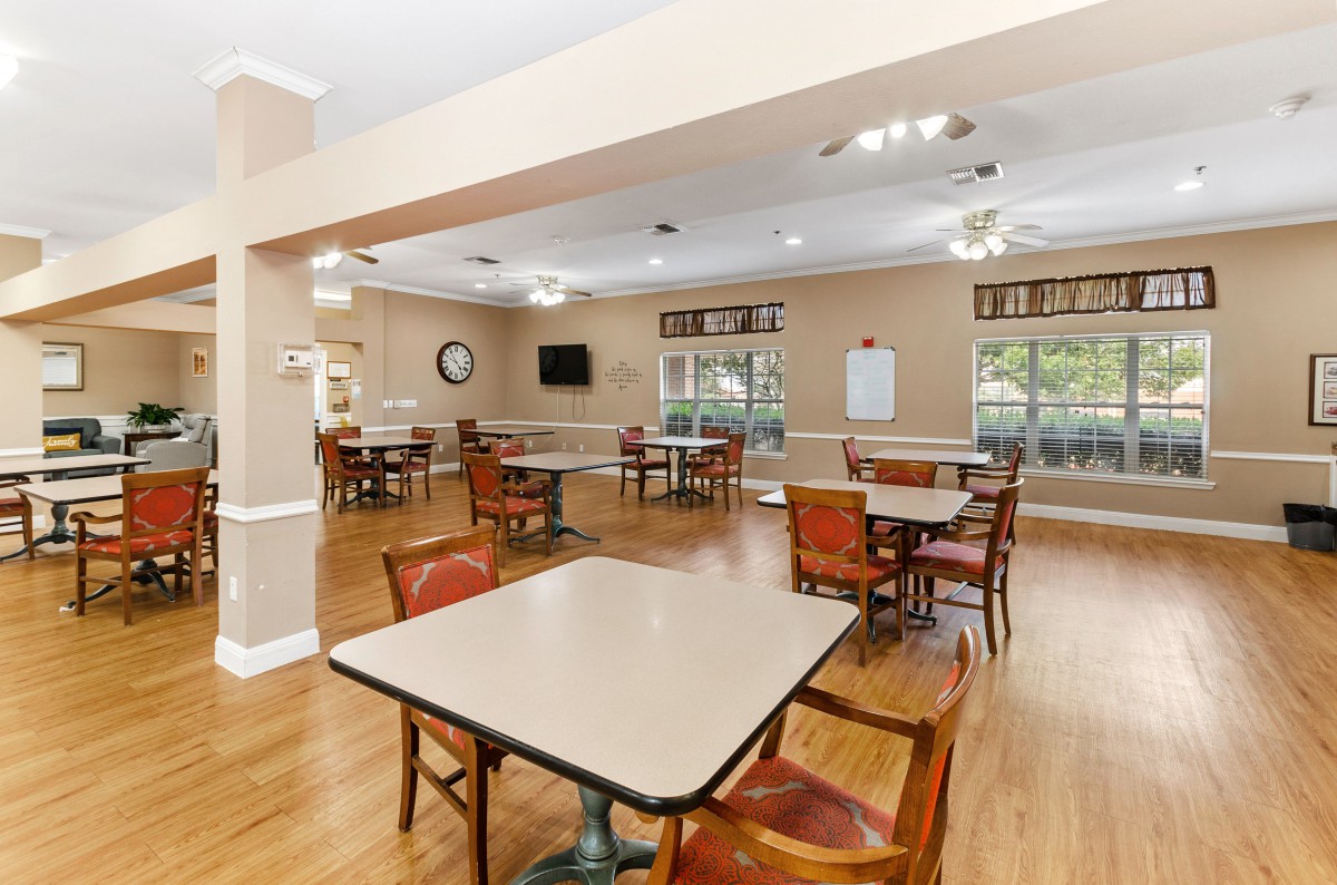 A spacious dining area with multiple tables and chairs, featuring wooden flooring and ample lighting.