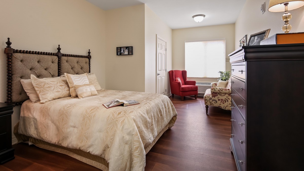 A cozy bedroom with a bed, red and patterned chairs, and large windows providing natural light.