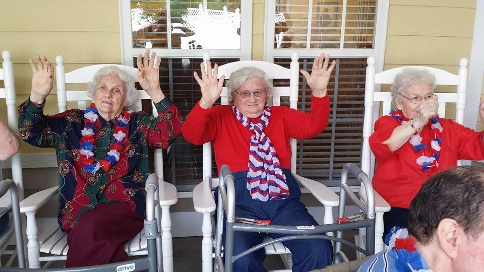 Elderly women in patriotic attire sitting on rocking chairs, raising their hands joyfully.
