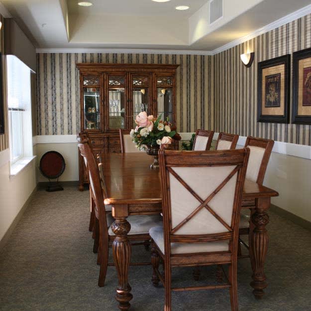 A traditional dining room with a long wooden table and matching chairs, accented by floral arrangements and elegant decor.