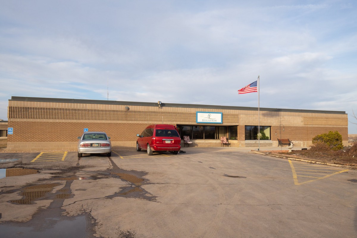 A school building with cars parked in front and an American flag flying overhead.