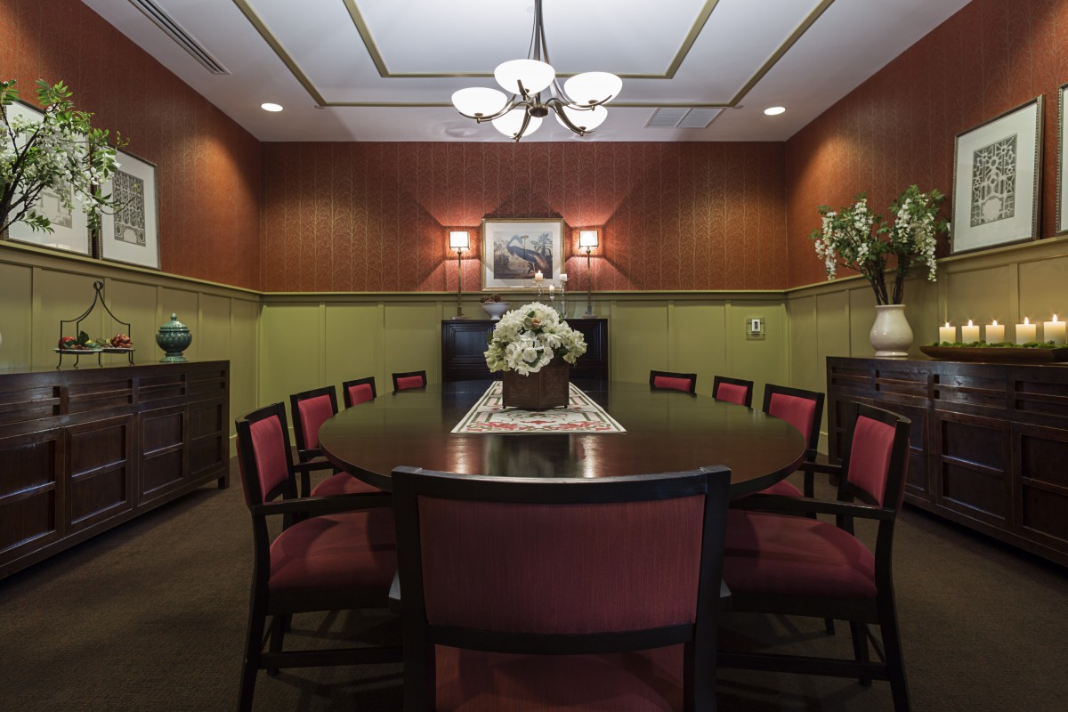 A formal conference room with a large oval table surrounded by chairs, adorned with floral arrangements and artwork.