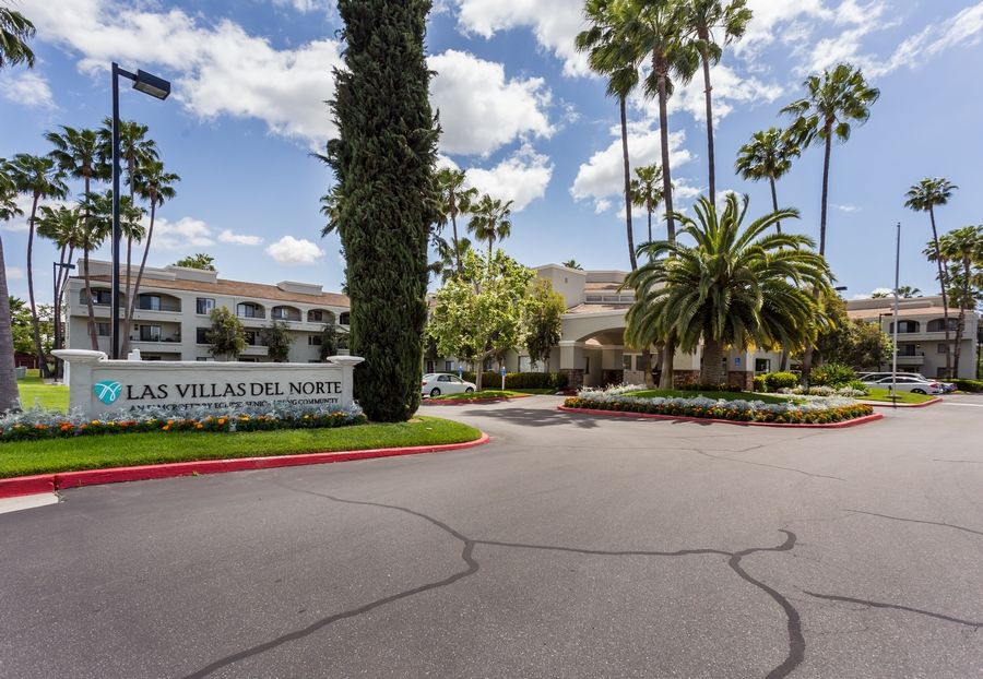 A scenic entrance to a resort with palm trees and well-maintained landscaping on a sunny day.