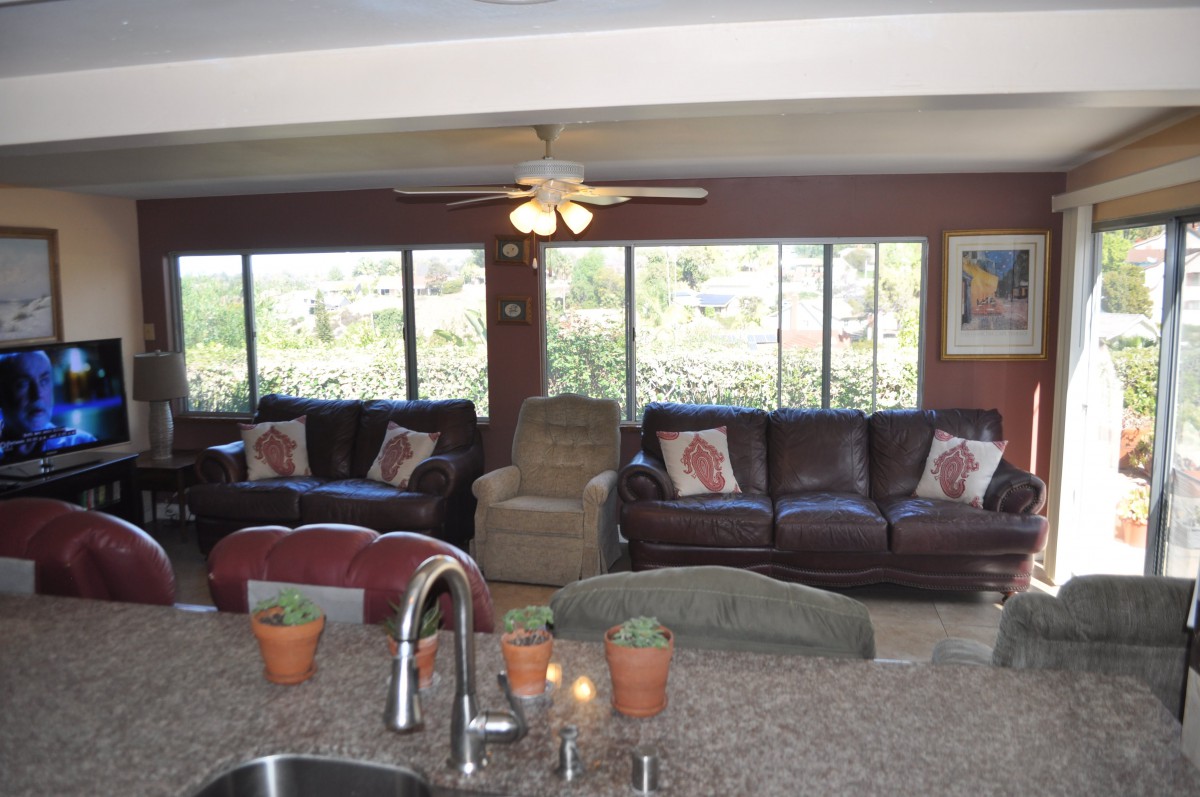 A cozy living room with large windows, sofas, and a ceiling fan.