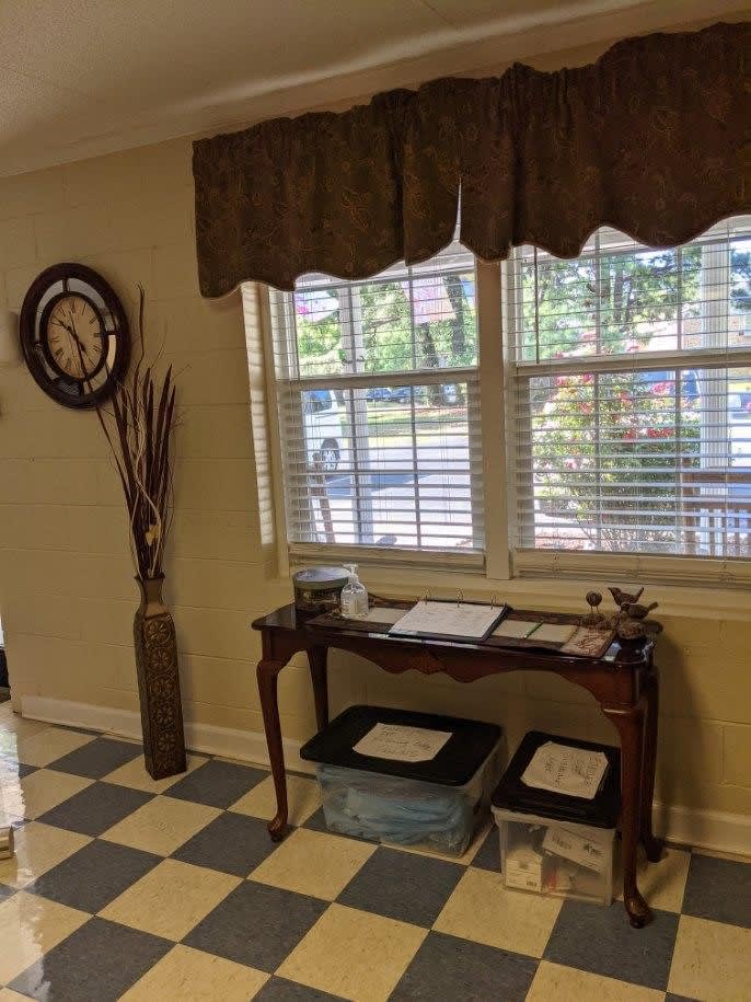A cozy waiting area with a table and clock beside a sunny window.
