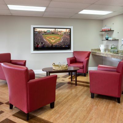 A cozy lounge area featuring red chairs, a flat-screen TV, and a small beverage station.