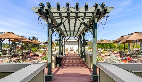 A scenic outdoor walkway under a wooden pergola leading to a garden area.