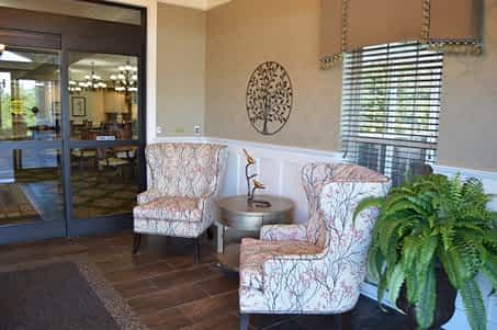 A cozy lobby with two patterned chairs, a small round table, decorative wall art, and a potted plant.