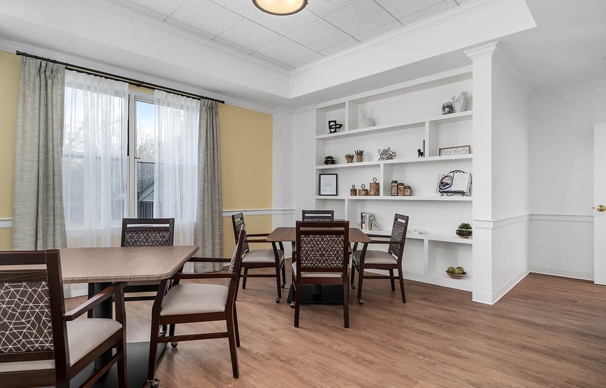 A modern dining area with wooden flooring, tables and chairs, and decorative shelves.
