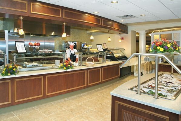 A clean and well-maintained cafeteria with a serving counter and kitchen staff.