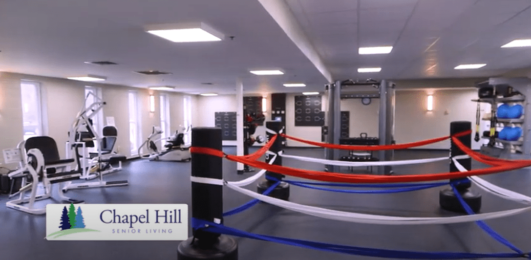 A modern boxing gym with a central boxing ring and various exercise equipment.