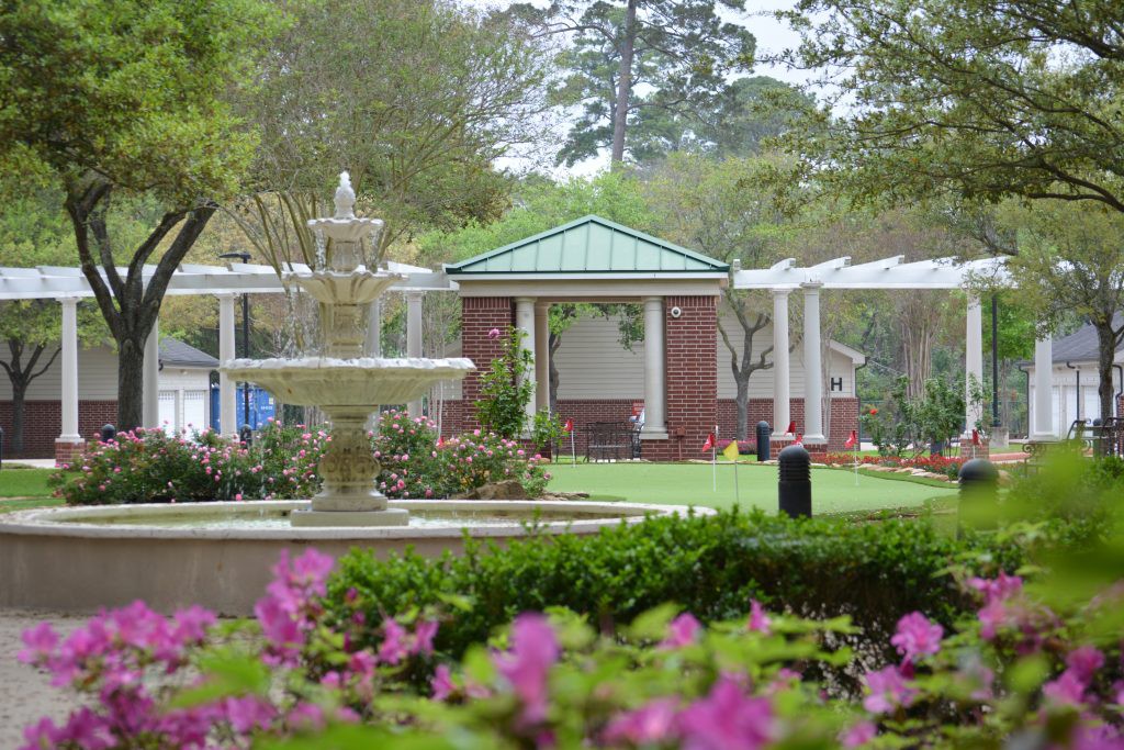 A serene garden scene featuring a fountain, vibrant flowers, and a gazebo in the background.