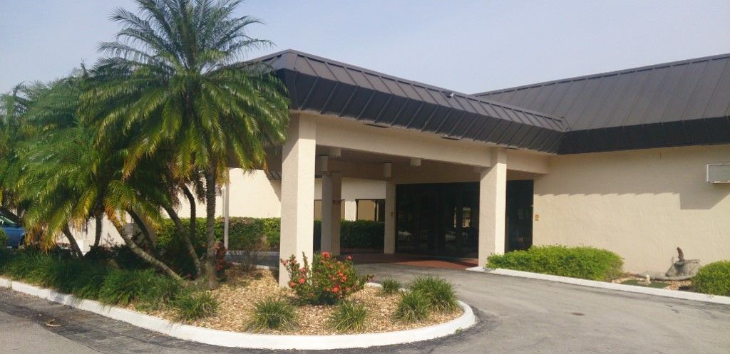 A building entrance with a covered driveway and landscaped area featuring a palm tree.