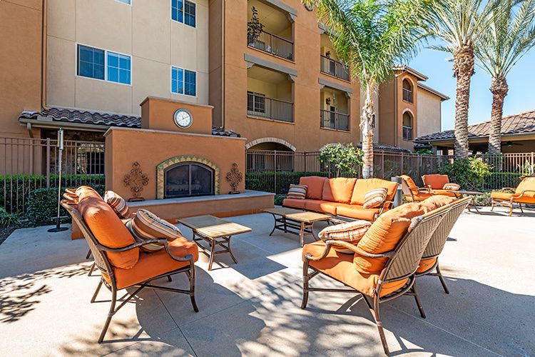 An outdoor patio area with comfortable seating and a fireplace in front of an apartment building.