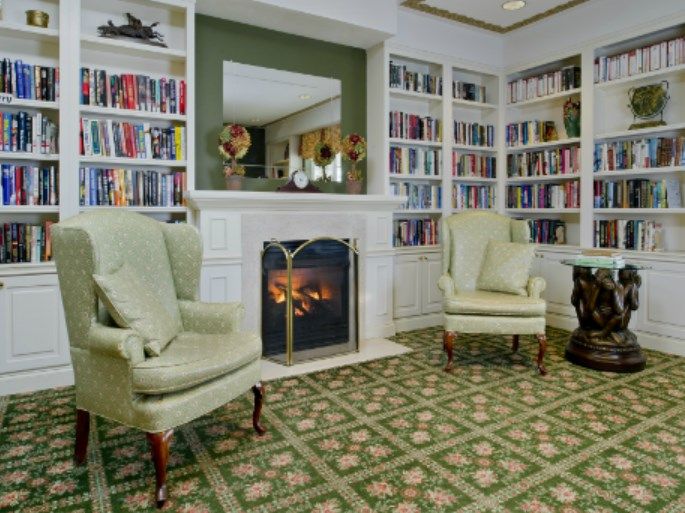 A cozy library with bookshelves, armchairs, and a fireplace.