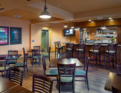 A cozy restaurant interior featuring a dining area with wooden tables, chairs, and a bar in the background.