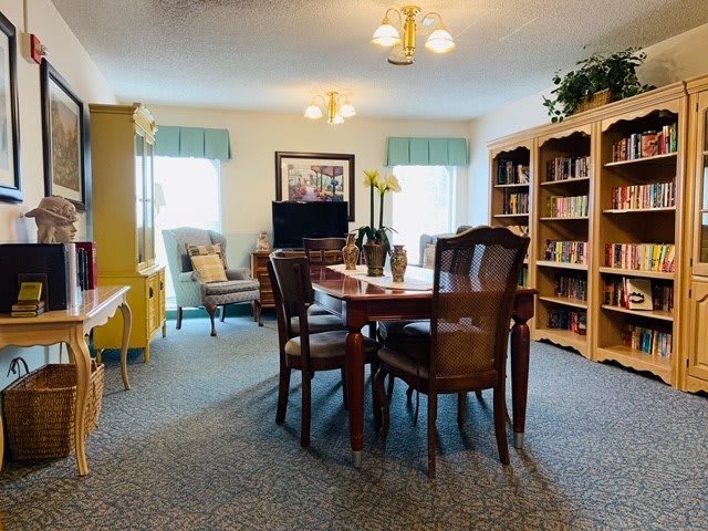 A cozy living space with bookshelves, a central table surrounded by chairs, and comfortable seating areas near the window.