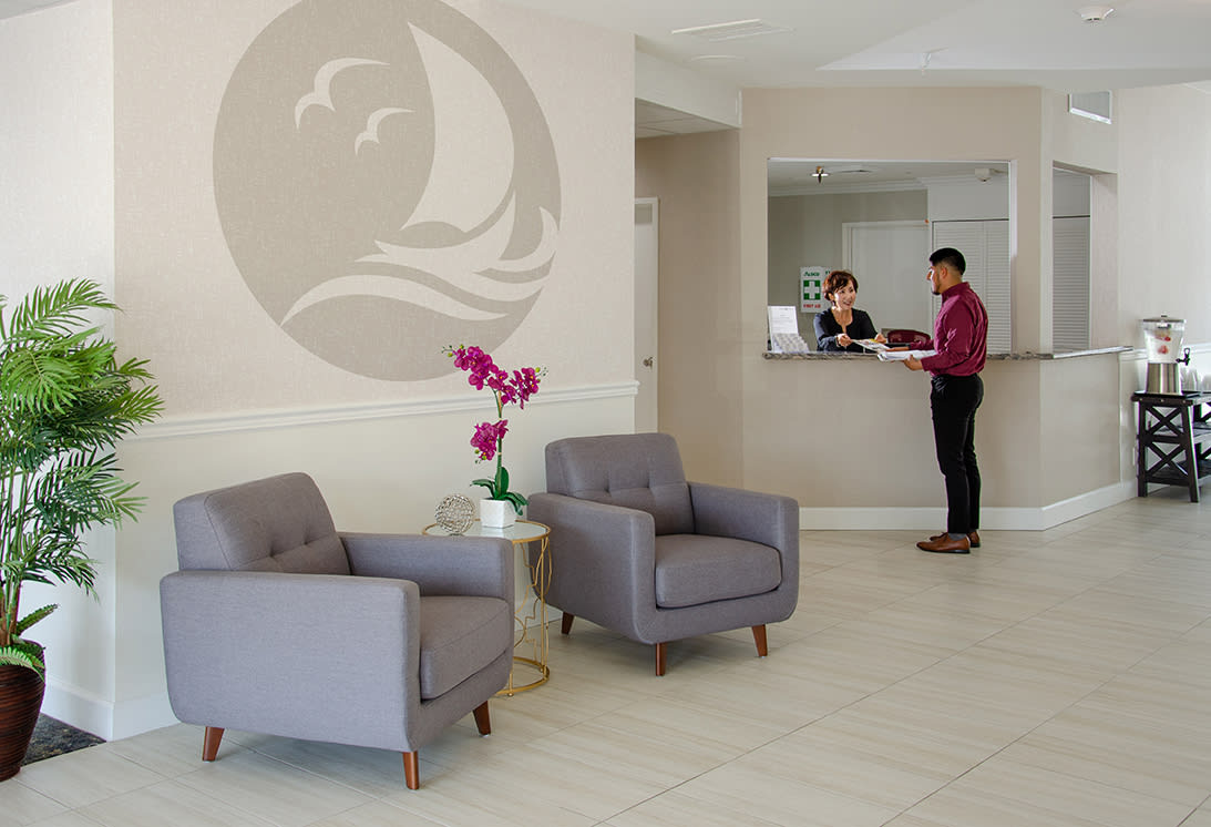A modern lobby with comfortable seating and a reception desk where two people are conversing.