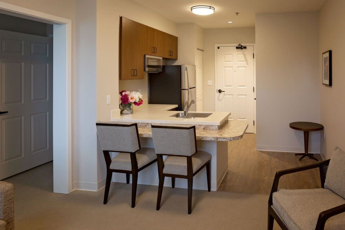 A modern kitchen area in an apartment with a countertop and chairs.