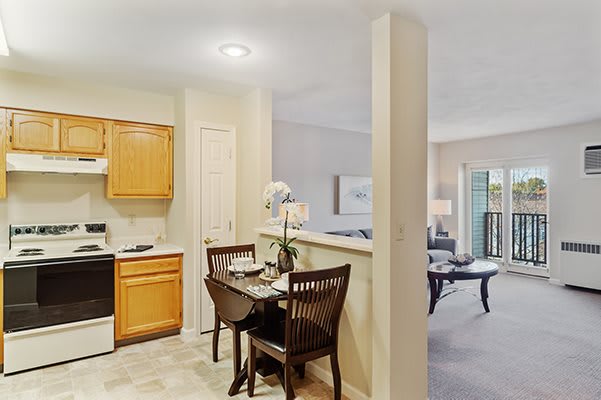 A cozy kitchen and dining area featuring wooden cabinets, a small dining table with chairs, and an open layout leading to the living room.