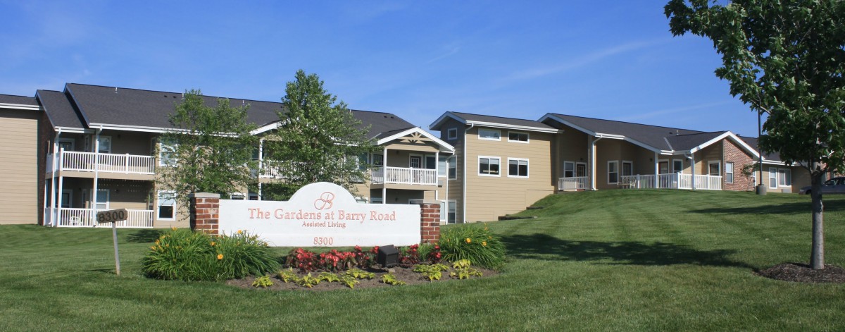 A sunny view of a residential apartment complex with well-maintained landscaping and a prominent entrance sign.