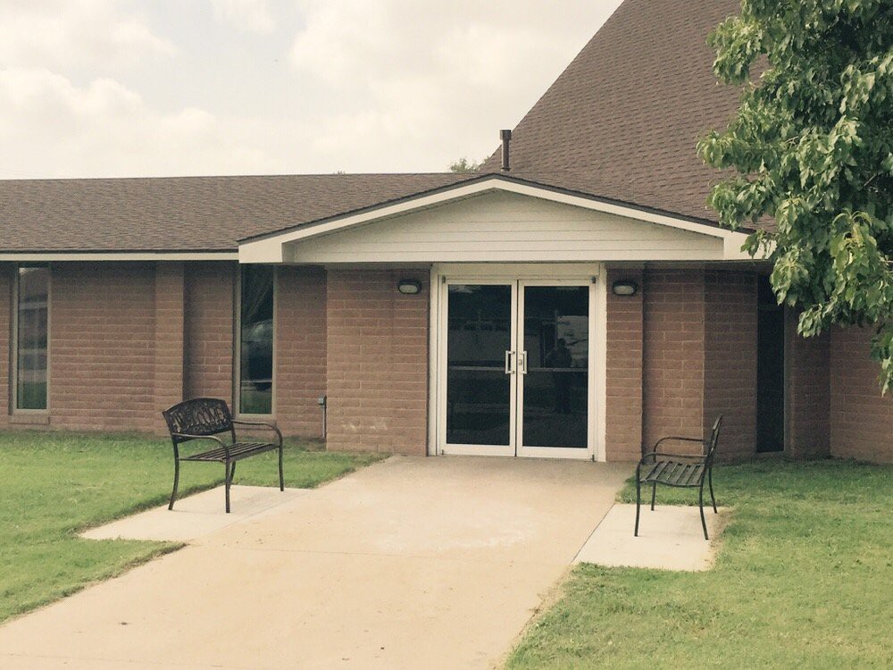 A brick building entrance with chairs on a sidewalk leading up to glass doors.