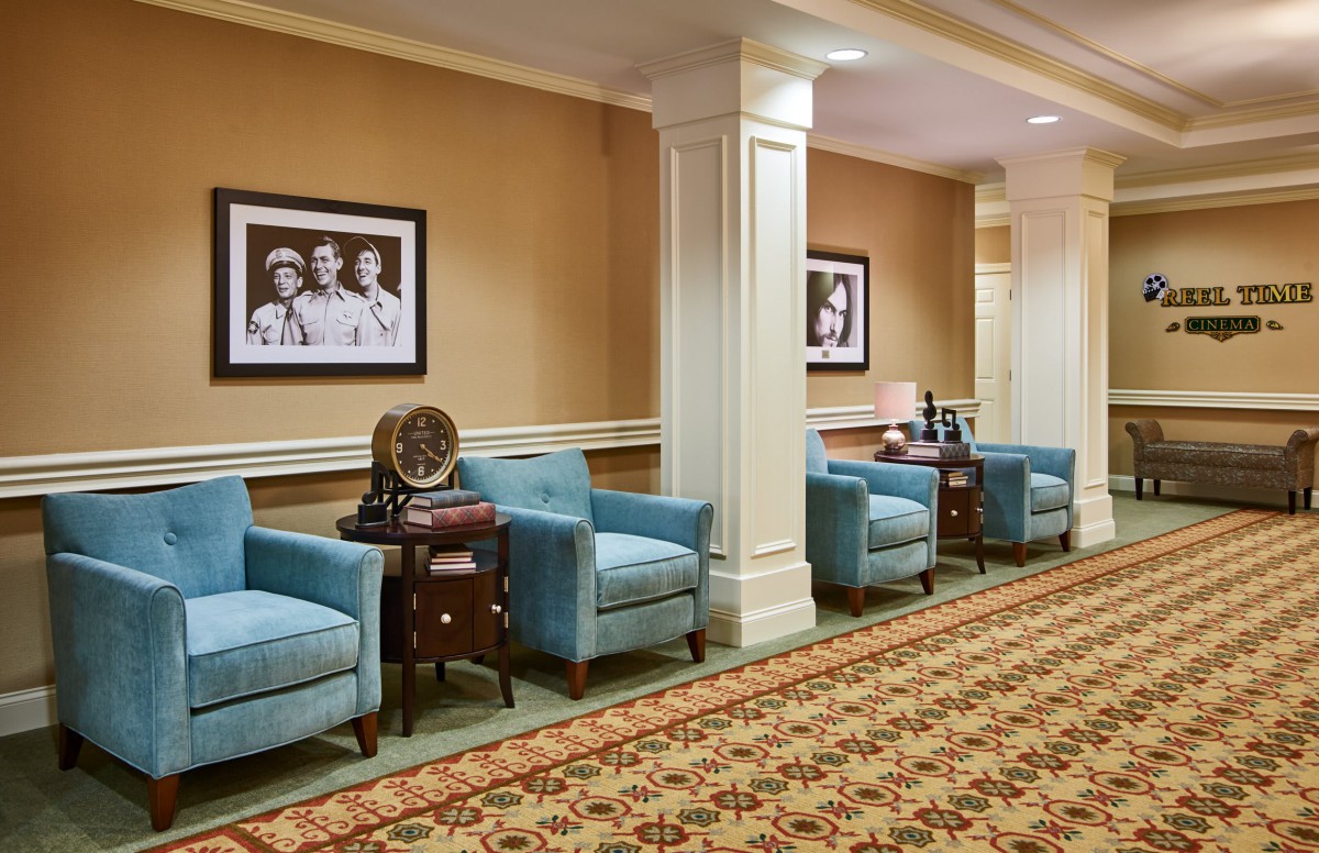 A cozy lobby area featuring blue armchairs, decorative tables, and framed artwork on the walls.
