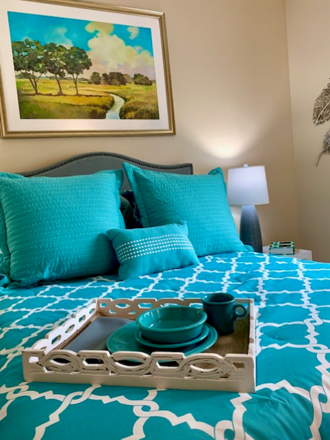 A cozy bedroom featuring turquoise bedding with matching pillows and a decorative tray set on the bed.