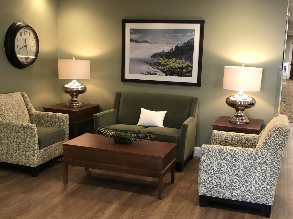 A cozy living room featuring a green sofa, armchairs, and a wooden coffee table, accented by decorative lamps and a landscape painting on the wall.