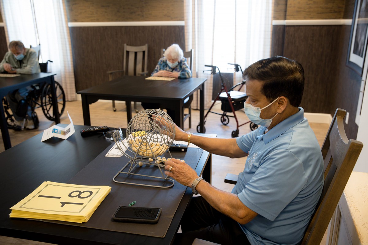 Two people engage in a bingo game, with one operating the bingo cage and numbers, while the other sits at a distance.