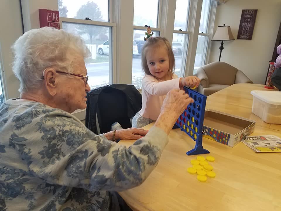 An elderly woman and a young girl enjoying a game of Connect Four together indoors.