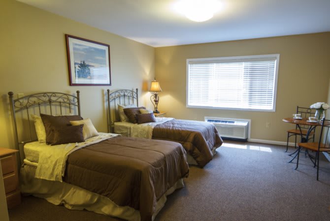 A cozy hotel room featuring two neatly made twin beds, a lamp, and a large window allowing natural light.