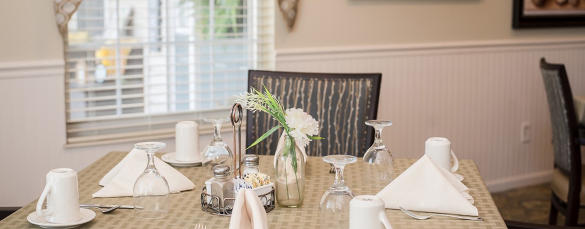 A neatly set dining table with glassware, folded napkins, and a vase of flowers.