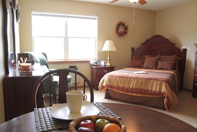 A cozy bedroom with a neatly made bed and a small dining area featuring a fruit basket.