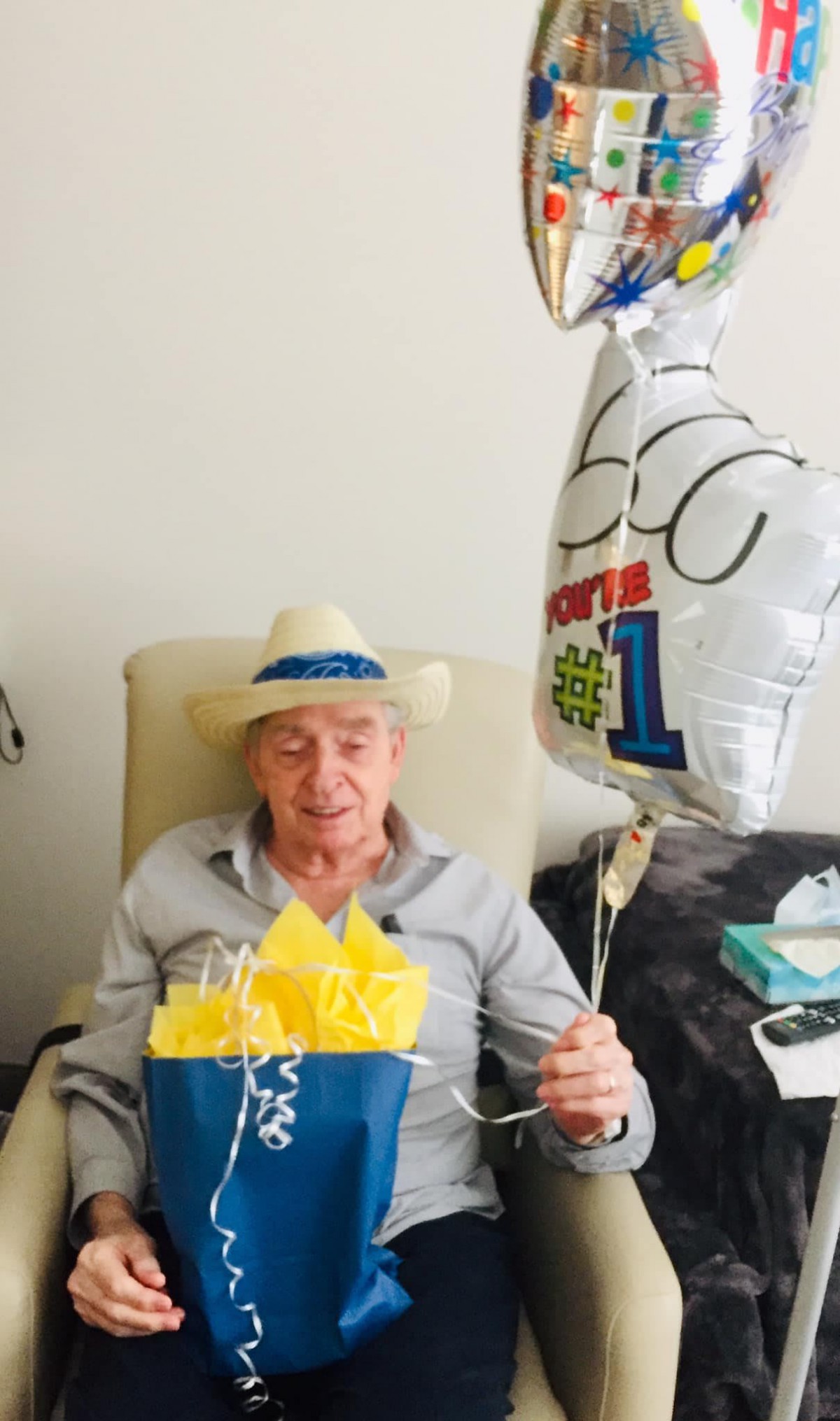 An elderly man celebrating his birthday with balloons and a gift bag.