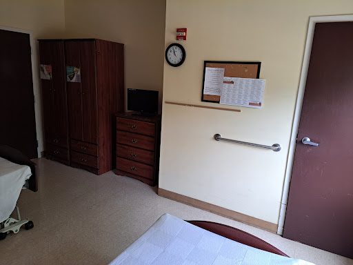 A view of a hospital room featuring a bed, clock, and storage furniture.