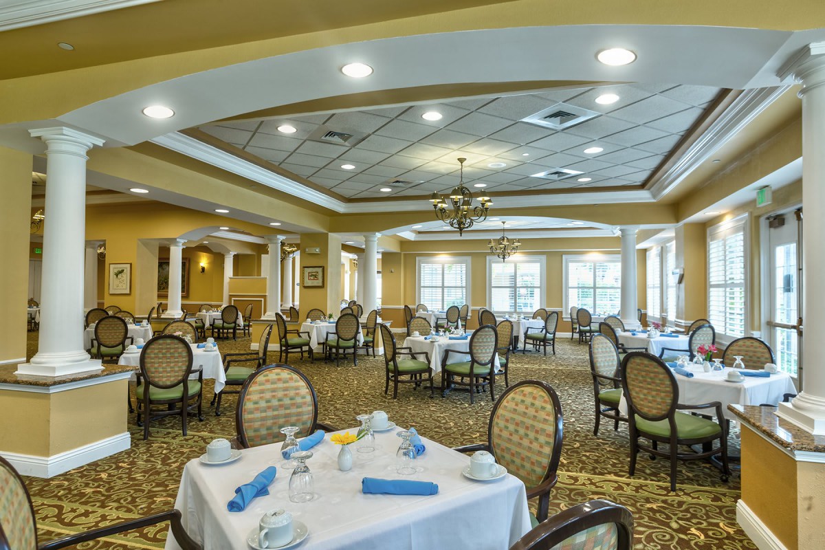 An elegant dining room with neatly arranged tables and chairs, featuring warm lighting and a formal atmosphere.