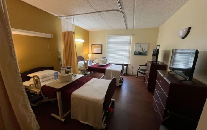 A hospital room with two beds separated by a curtain, featuring various furnishings and medical equipment.