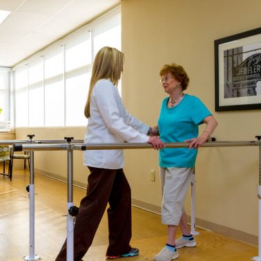 A rehabilitation specialist assists an elderly woman during a physical therapy session.