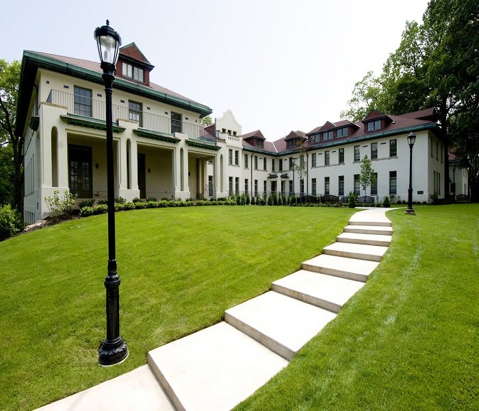 A grand mansion with a well-maintained lawn and a stone pathway leading to the entrance.
