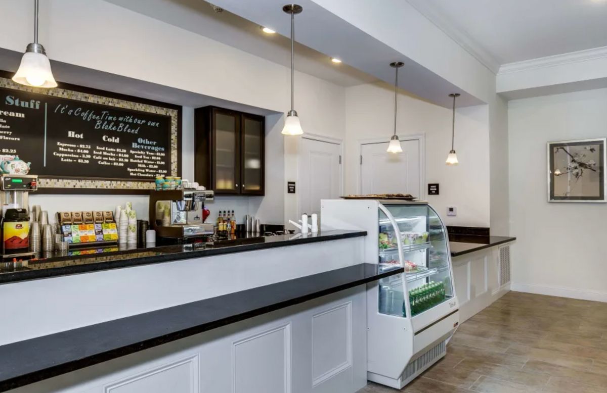 A modern cafe with a sleek counter and display case, featuring a menu board and pendant lighting.