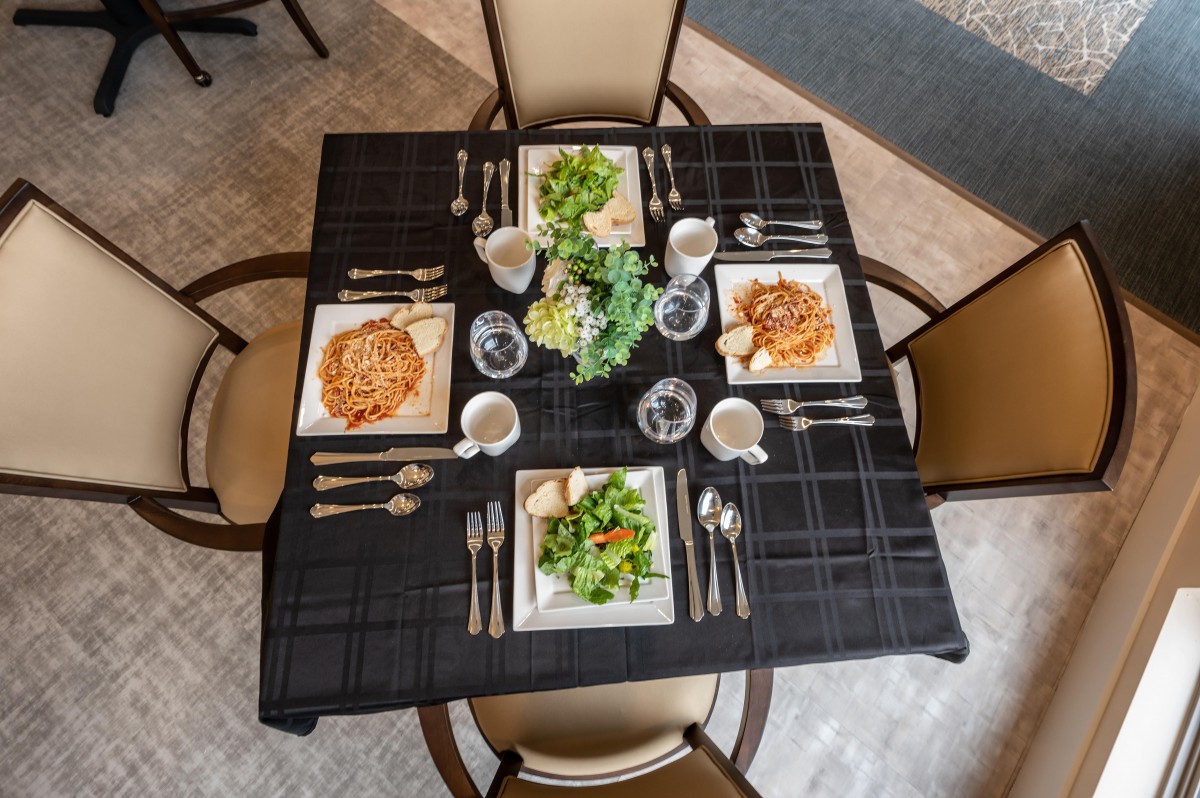 A top-down view of a restaurant table set for two with salads and pasta dishes.
