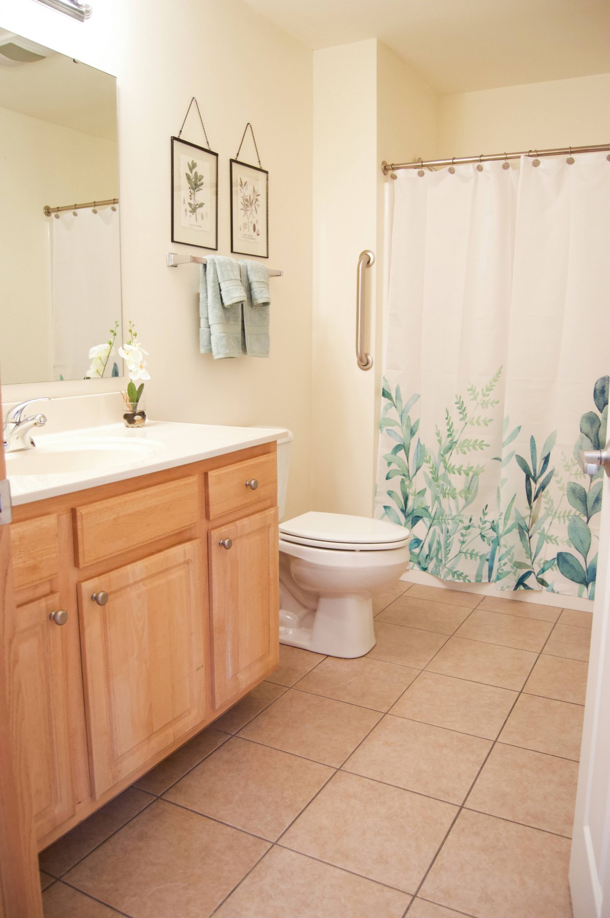 A clean and well-organized bathroom with a floral shower curtain and wooden cabinets.