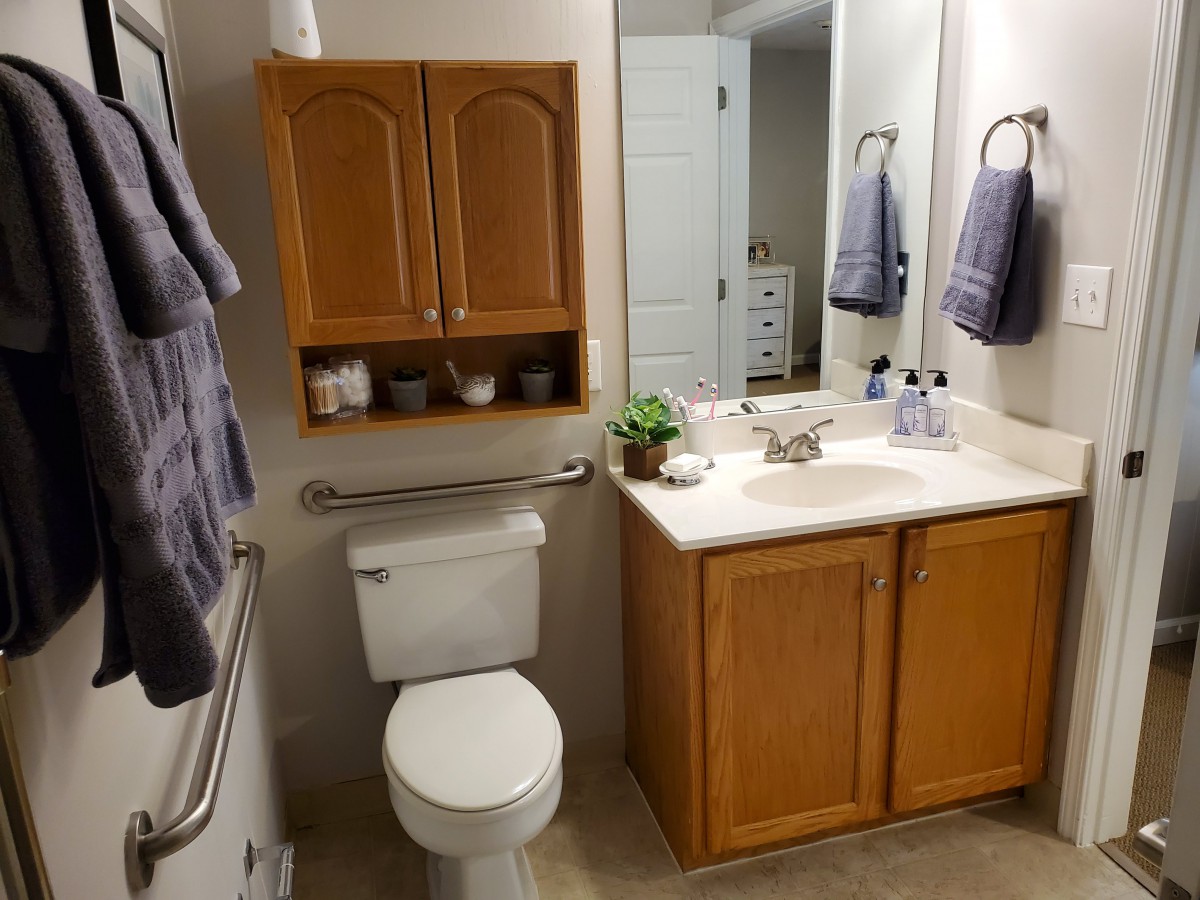 A clean and organized bathroom featuring a toilet, sink with mirror, wooden cabinet, and neatly arranged towels.