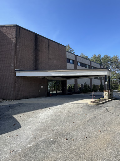 A modern commercial building with a covered entrance, surrounded by greenery on a clear day.