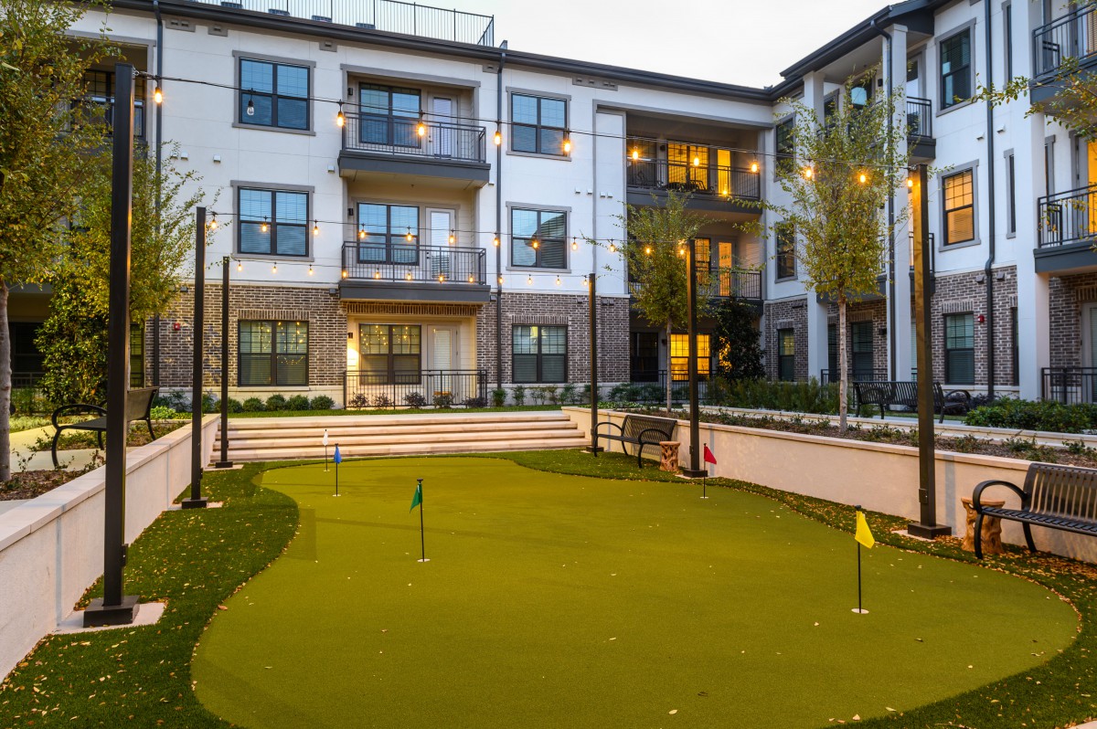 Modern apartment complex with a well-maintained putting green in the courtyard at dusk.